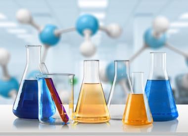 five various sized beakers and vials with colored toxic chemicals in a lab setting