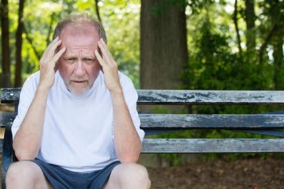 sad older man on park bench holding his head