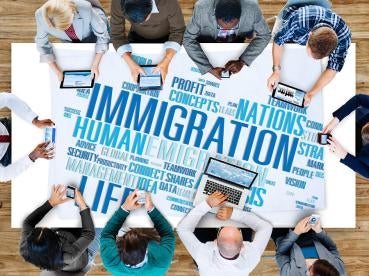 diverse group of individuals with various devices sitting around a table labeled with a Immigration, Nations, Human, word cloud