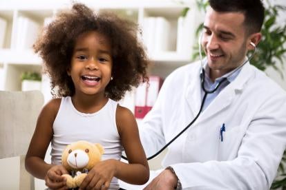 happy doctor or pediatrician using a stethoscope to examine a happy child holding a teddy bear during her checkup