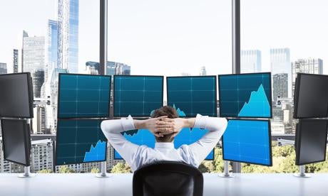 investment services professional appearing suspiciously laid back in front of 12 monitors with 8 showing uptrends in activity