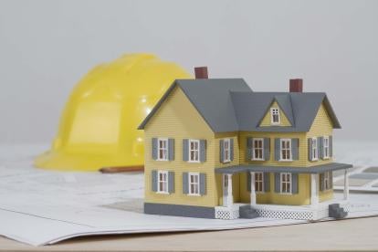 a toy sized model single family home sitting on blueprints with yellow construction hardhat