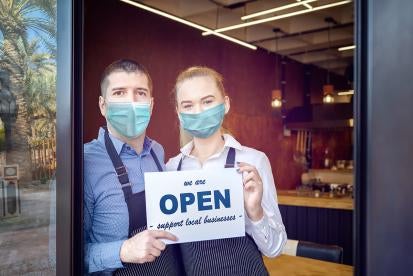 Open sign in business window with owners wearing masks 