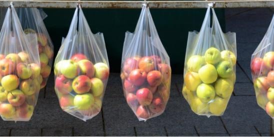 fresh green and red apples hanging in batches for sale in clear plastic bags
