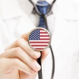 Doctor in a lab coat holding up stethoscope with an american flag illustrating U.S. Healthcare system 